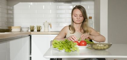 Woman sitting at table preparing fresh vegetables in a modern kitchen, highlighting healthy living and independence.