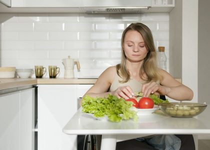Woman sitting at table preparing fresh vegetables in a modern kitchen, highlighting healthy living and independence.