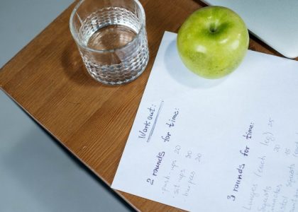 A green apple, glass of water, and workout plan on a wooden desk symbolize healthy living.