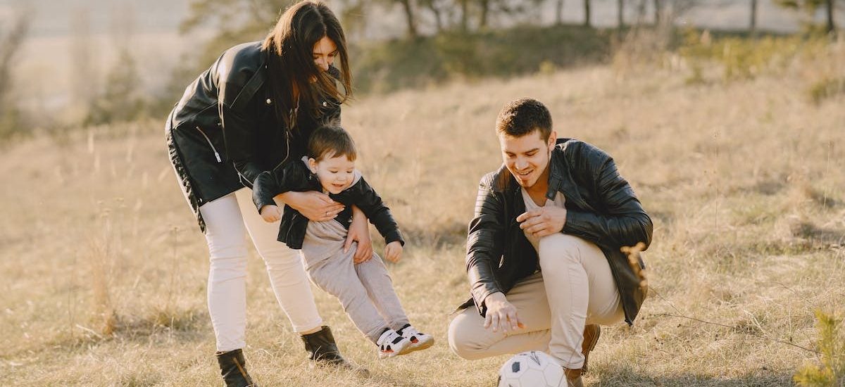A happy family playing with a soccer ball in a grassy field on a sunny day.