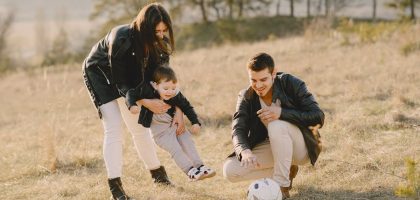 A happy family playing with a soccer ball in a grassy field on a sunny day.