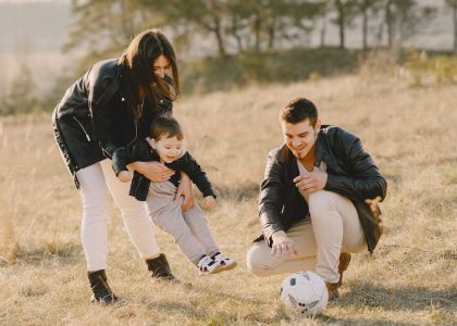 A happy family playing with a soccer ball in a grassy field on a sunny day.